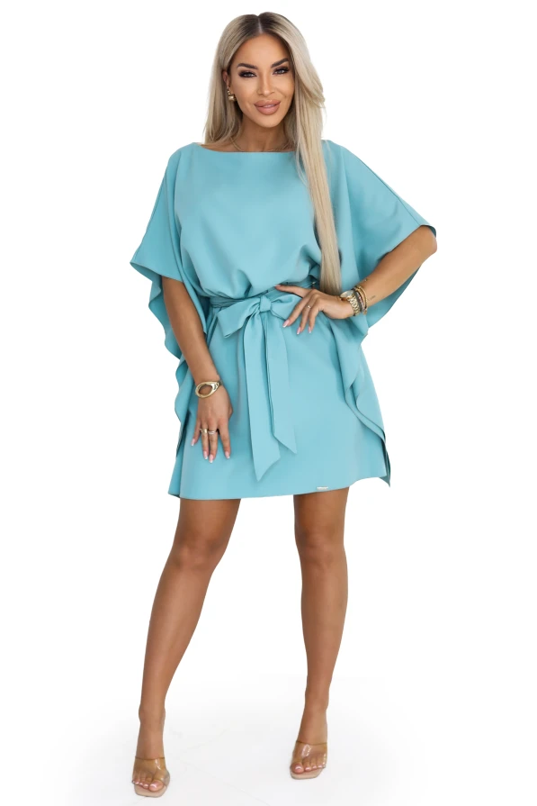 Modelis turkio spalvos Numoco mini suknelėje su šikšnosparnio tipo rankovėmis ir juosmenyje surištu diržu.