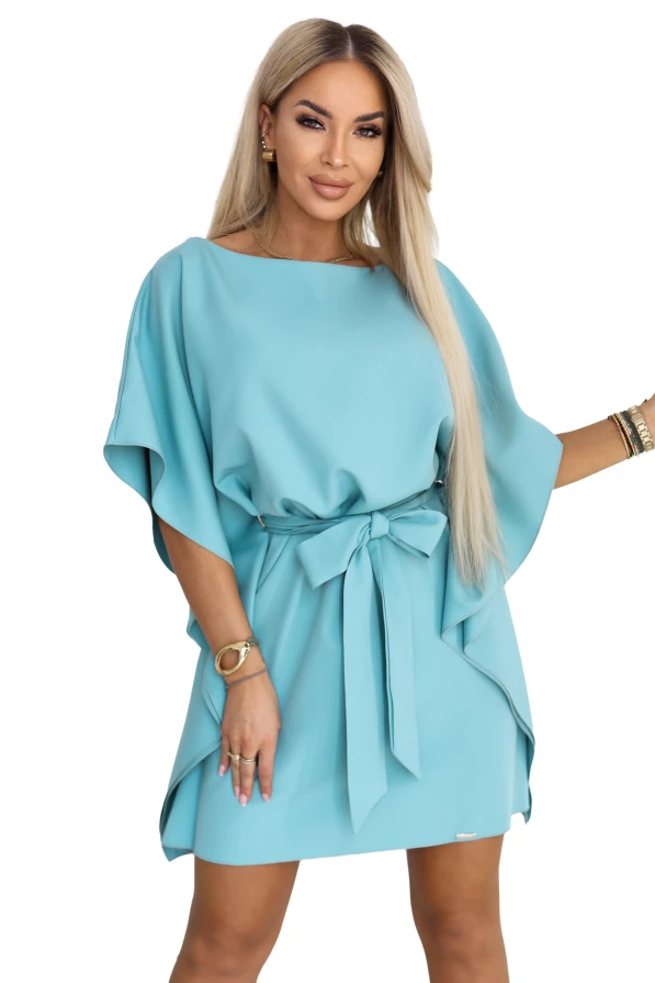 Modelis turkio spalvos Numoco mini suknelėje su šikšnosparnio tipo rankovėmis ir juosmenyje surištu diržu.