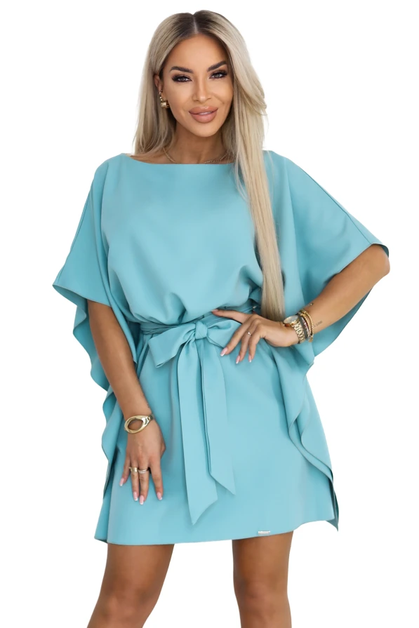 Modelis turkio spalvos Numoco mini suknelėje su šikšnosparnio tipo rankovėmis ir juosmenyje surištu diržu.