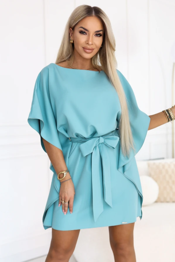 Modelis turkio spalvos Numoco mini suknelėje su šikšnosparnio tipo rankovėmis ir juosmenyje surištu diržu.