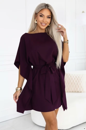 Modelė su Numoco kimono tipo suknele prinokusių slyvų spalvos, su valties formos iškirpte, plačiomis rankovėmis, liemenyje užrišama juosta ir drapiruotais šonais, iki kelių ilgio.}