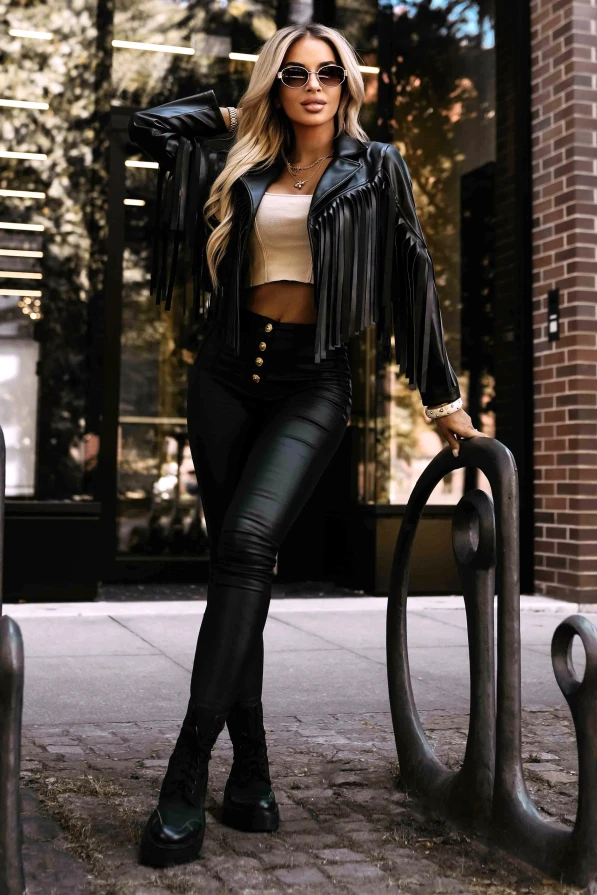 Modelka w czarnej ramonesce z frędzlami od Numoco Basic pozuje na tle nowoczesnej architektury, podkreślając modny i odważny charakter stylizacji.