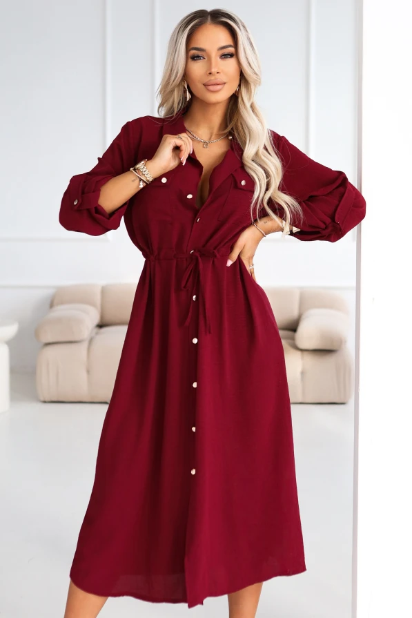 Elegancka stylizacja: modelka prezentuje bordową sukienkę midi typu shirt dress z kieszeniami na piersi, w jasnym wnętrzu glamour.